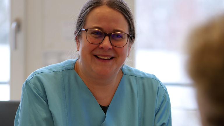Dr. med. Saskia Otte, Chefärztin der Geriatrie & Physikalischen Medizin, sitzt an einem Schreibtisch in blauer Funktionskleidung und unterhält sich mit einer ihr gegenüber sitzenden Person im Amalie Sieveking Krankenhaus in Hamburg-Volksdorf Dr. med. Saskia Otte, Chefärztin der Geriatrie & Physikalischen Medizin, sitzt an einem Schreibtisch in blauer Funktionskleidung und unterhält sich mit einer ihr gegenüber sitzenden Person im Amalie Sieveking Krankenhaus in Hamburg-Volksdorf