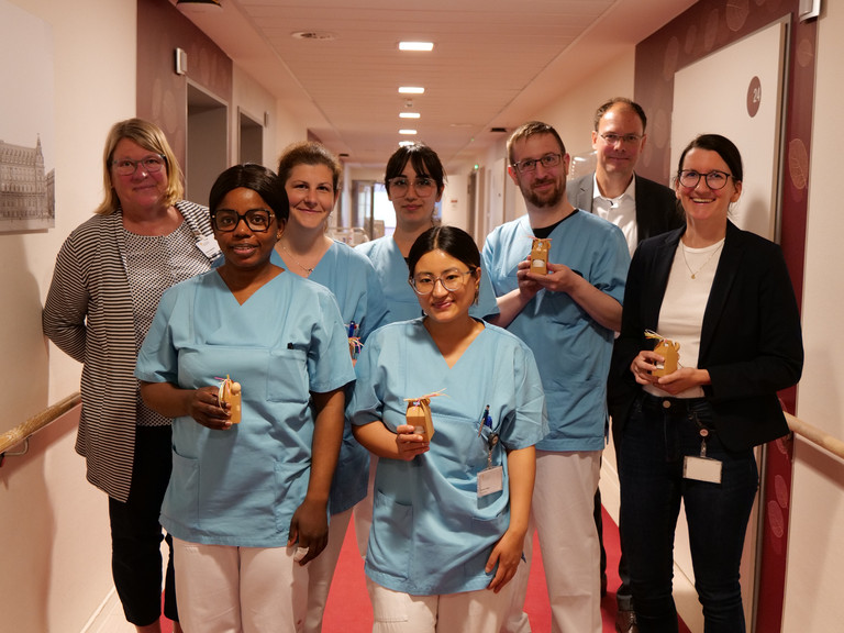 Mehrere Pflegekräfte in blauer Funktionskleidung halten kleine Präsente in den Händen und stehen mit Pflegedirektorin Maike Sellentin, ihrer Stellvertretrin Sabrina Oberle und Krankenhausgeschäftsführer Andreas Schneider in einem Krankenhausflur zum Internationalen Tag der Pflegenden 2026. Mehrere Pflegekräfte in blauer Funktionskleidung halten kleine Präsente in den Händen und stehen mit Pflegedirektorin Maike Sellentin, ihrer Stellvertretrin Sabrina Oberle und Krankenhausgeschäftsführer Andreas Schneider in einem Krankenhausflur zum Internationalen Tag der Pflegenden 2026.