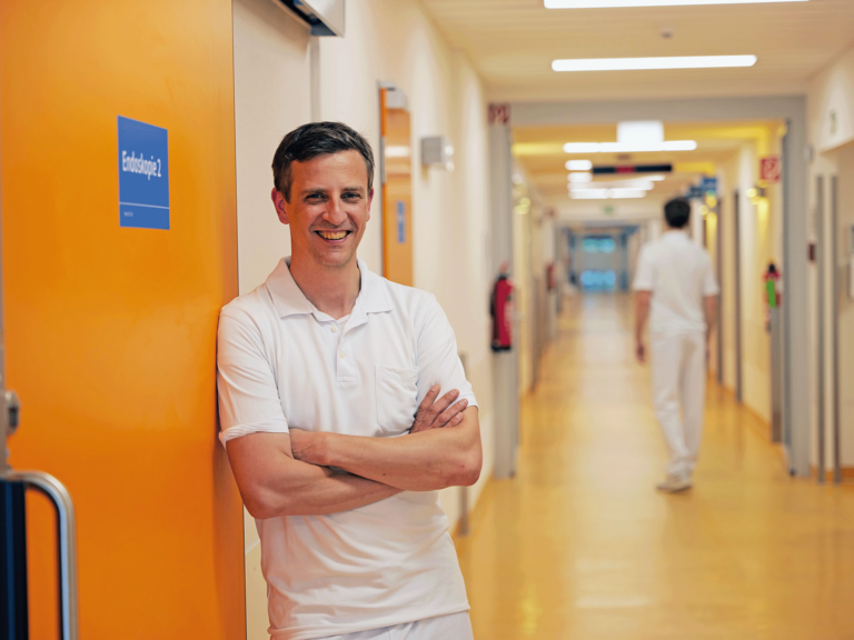 Priv.-Doz. Dr. med. Johannes Kluwe, Chefarzt der Allgemeinen Inneren Medizin und Gastroenterologie am Evangelischen Amalie Sieveking Krankenhaus, steht in weißer Funktionskleidung an einer Schiebetür zur Endoskopie in einem Stationsflur und blickt in die Kamera. Priv.-Doz. Dr. med. Johannes Kluwe, Chefarzt der Allgemeinen Inneren Medizin und Gastroenterologie am Evangelischen Amalie Sieveking Krankenhaus, steht in weißer Funktionskleidung an einer Schiebetür zur Endoskopie in einem Stationsflur und blickt in die Kamera.