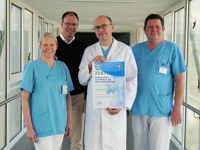Vier Mitarbeitende des Evangelischen Amalie Sieveking Krankenhauses stehen nebeneinander und präsentieren die DGAV-Zertifizierung für das Zentrum für Endokrine Chirurgie: Dr. Denise Wittek, Geschäftsführer Andreas Schneider, Prof. Dr. Ernst von Dobschütz und Oberarzt Alexander Gnoss. Vier Mitarbeitende des Evangelischen Amalie Sieveking Krankenhauses stehen nebeneinander und präsentieren die DGAV-Zertifizierung für das Zentrum für Endokrine Chirurgie: Dr. Denise Wittek, Geschäftsführer Andreas Schneider, Prof. Dr. Ernst von Dobschütz und Oberarzt Alexander Gnoss.